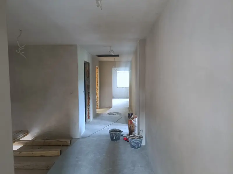 Korytarz w trakcie prac: wiadra, mieszadło do zaprawy, światło z końca korytarza