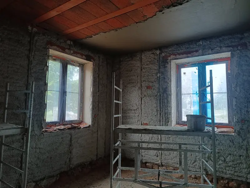 Ściany z odsłoniętym murem wokół okien, rusztowanie i narzędzia w pomieszczeniu